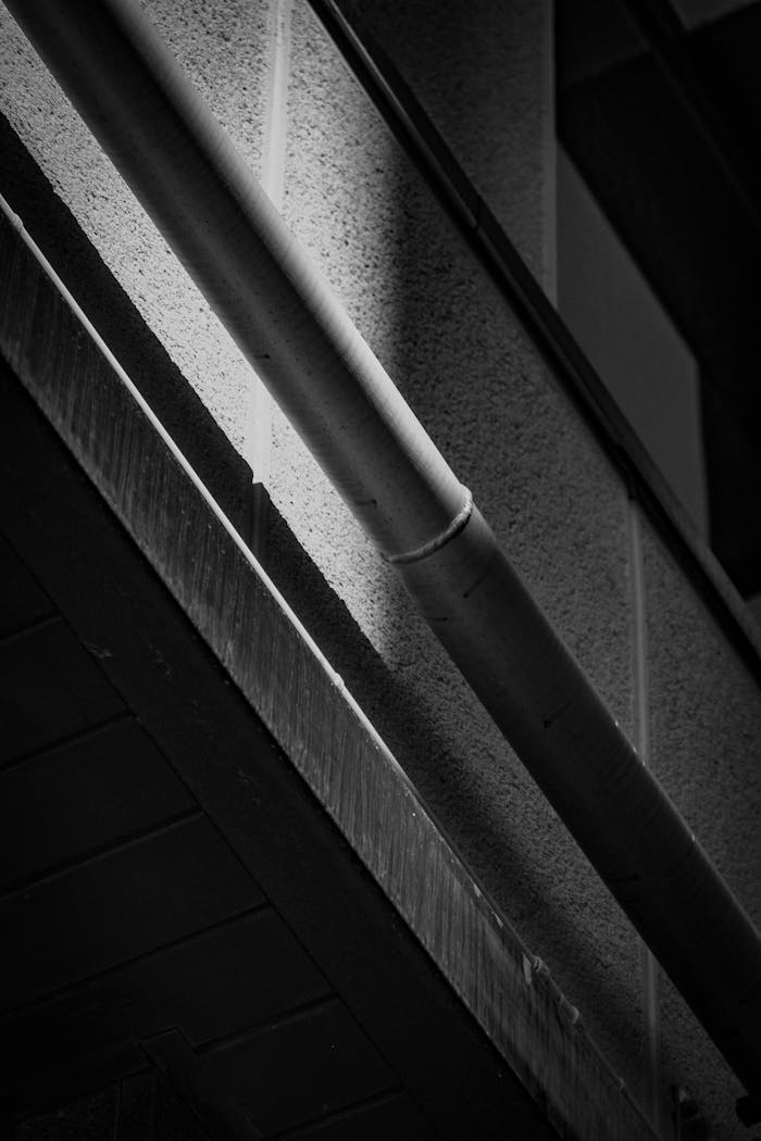 Black and white photo of an industrial pipe against a modern building. Ideal for construction themes.